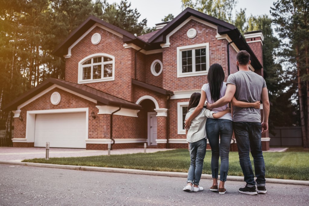 Back view of a happy family hugging in front of their modern home